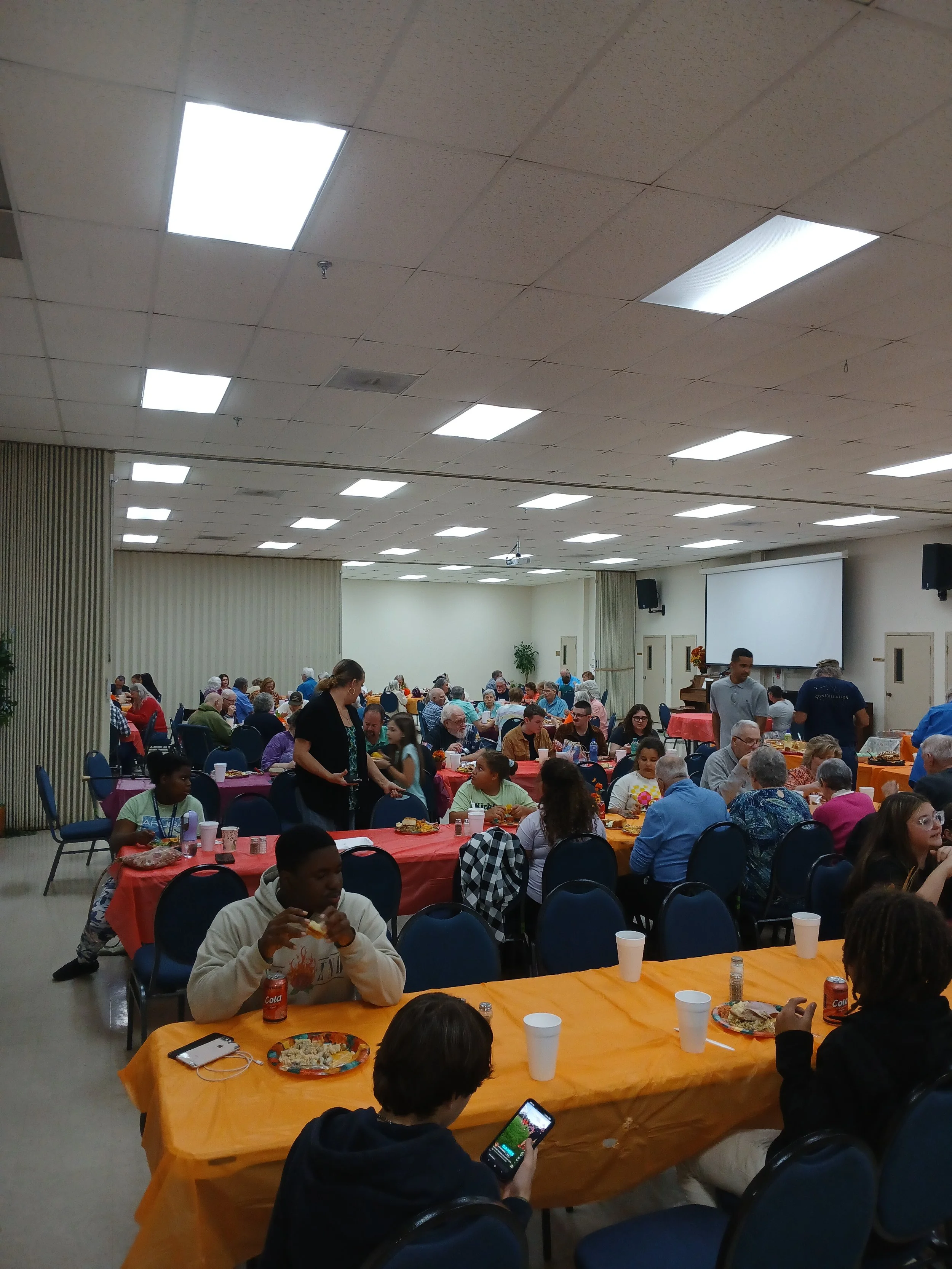 People gathered in a large banquet hall eating and socializing at decorated tables.