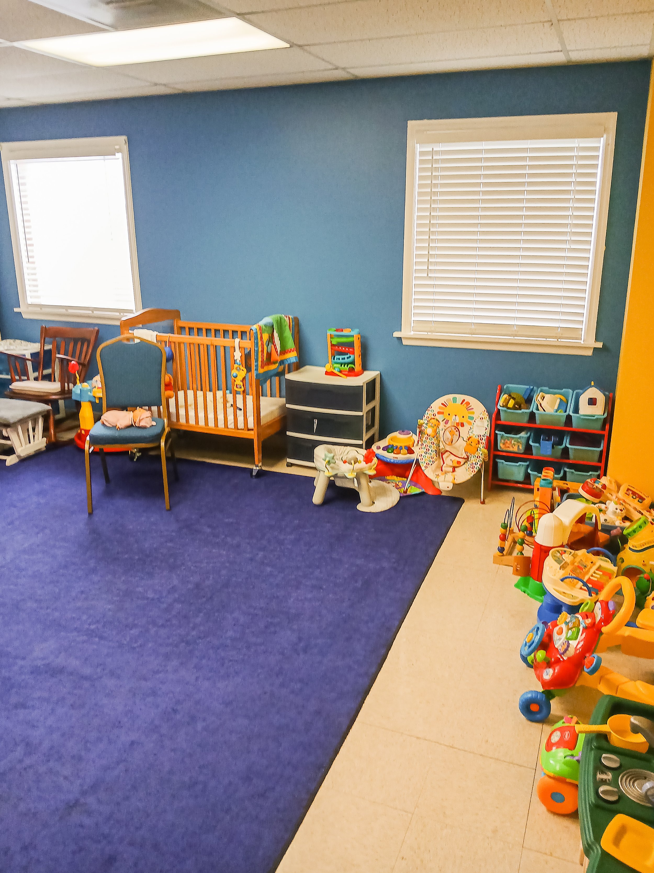 A playroom with blue walls, a blue carpet, and toys arranged along the walls.