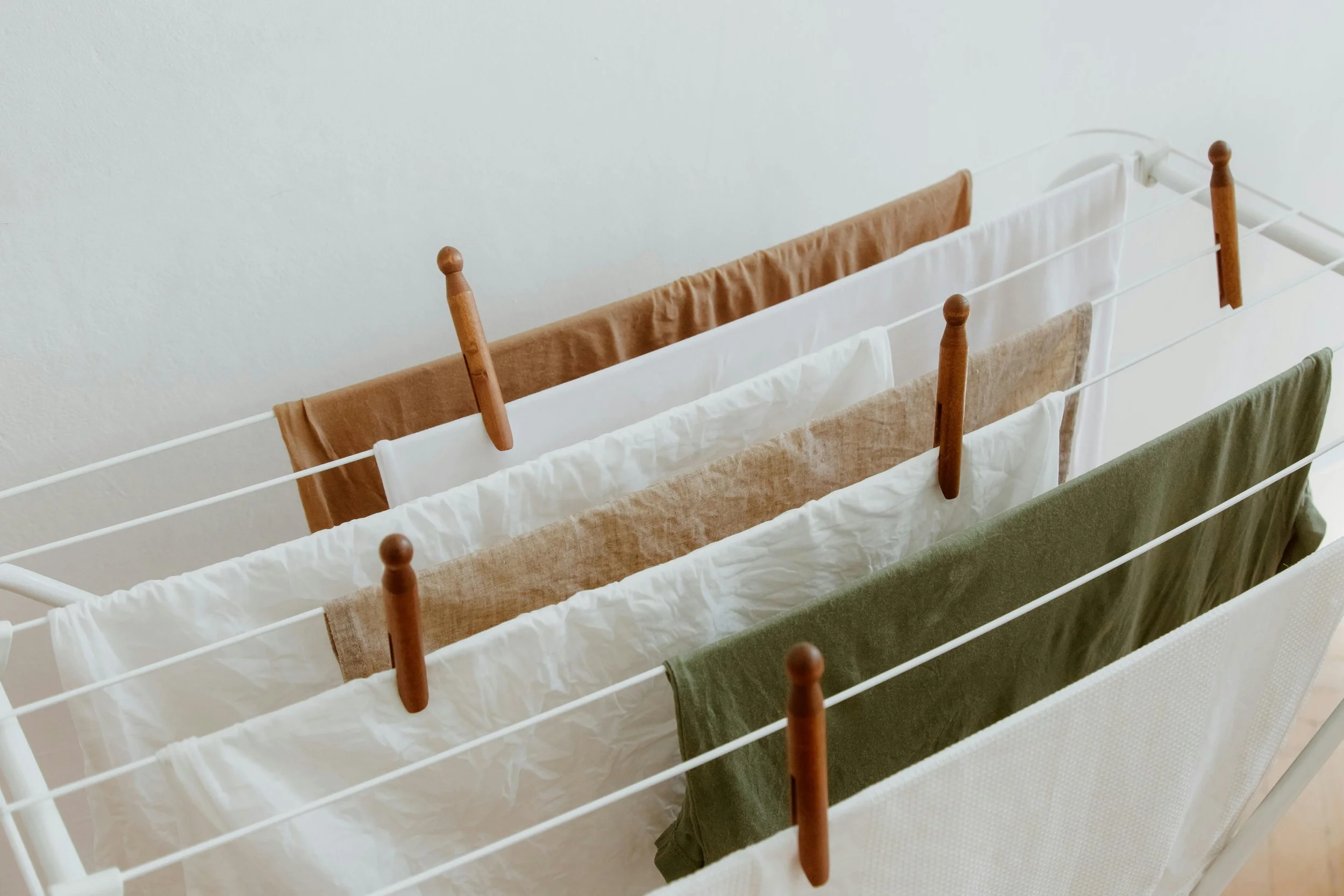 Clothes drying on a white rack with wooden pegs, including brown, white, beige, green, and cream garments