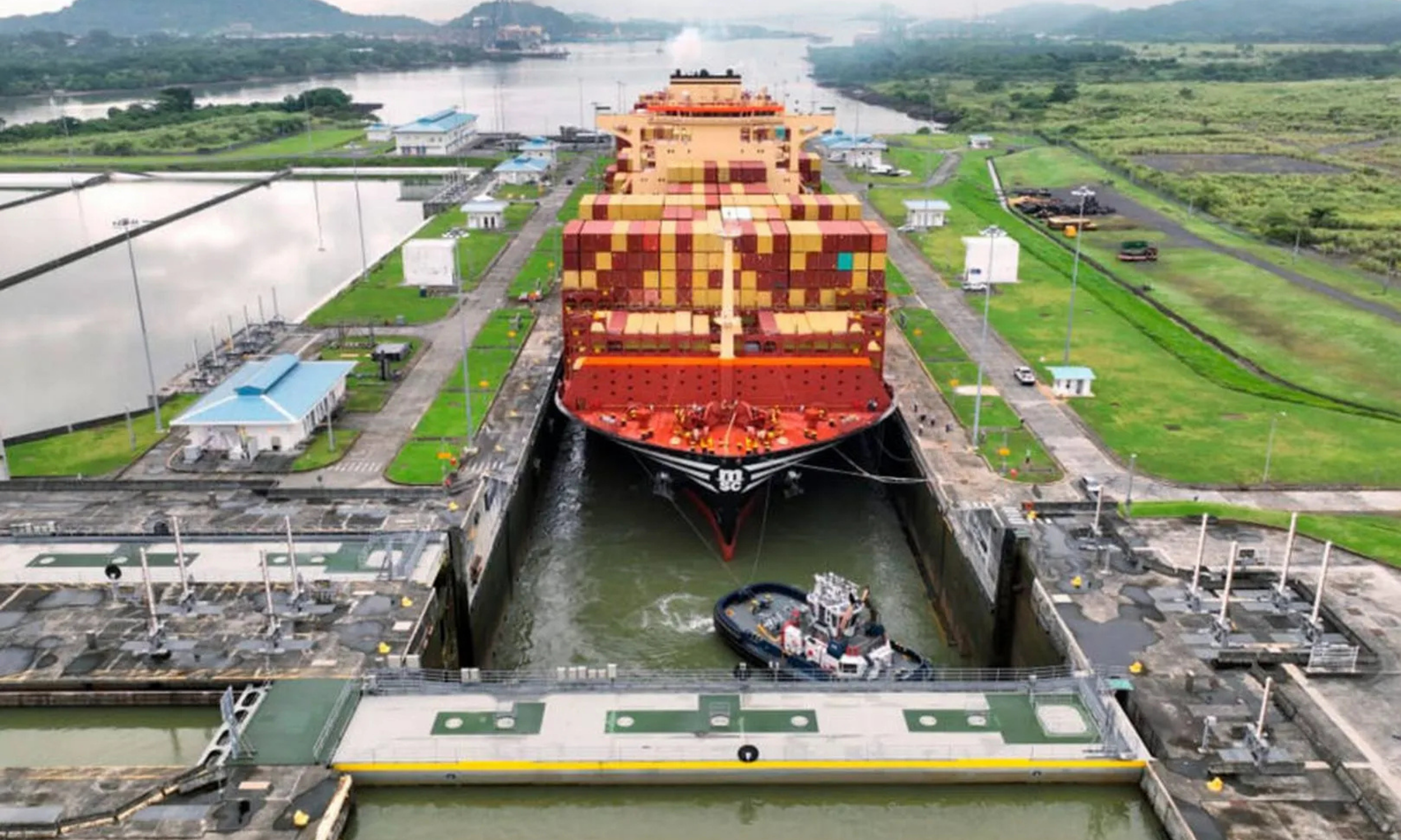 Aerial view of a large cargo ship passing through the Panama Canal locks surrounded by tropical jungle