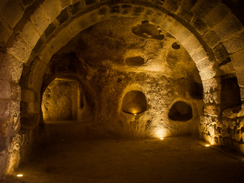 Underground cave with arched stone ceiling and rock walls illuminated by soft lighting.