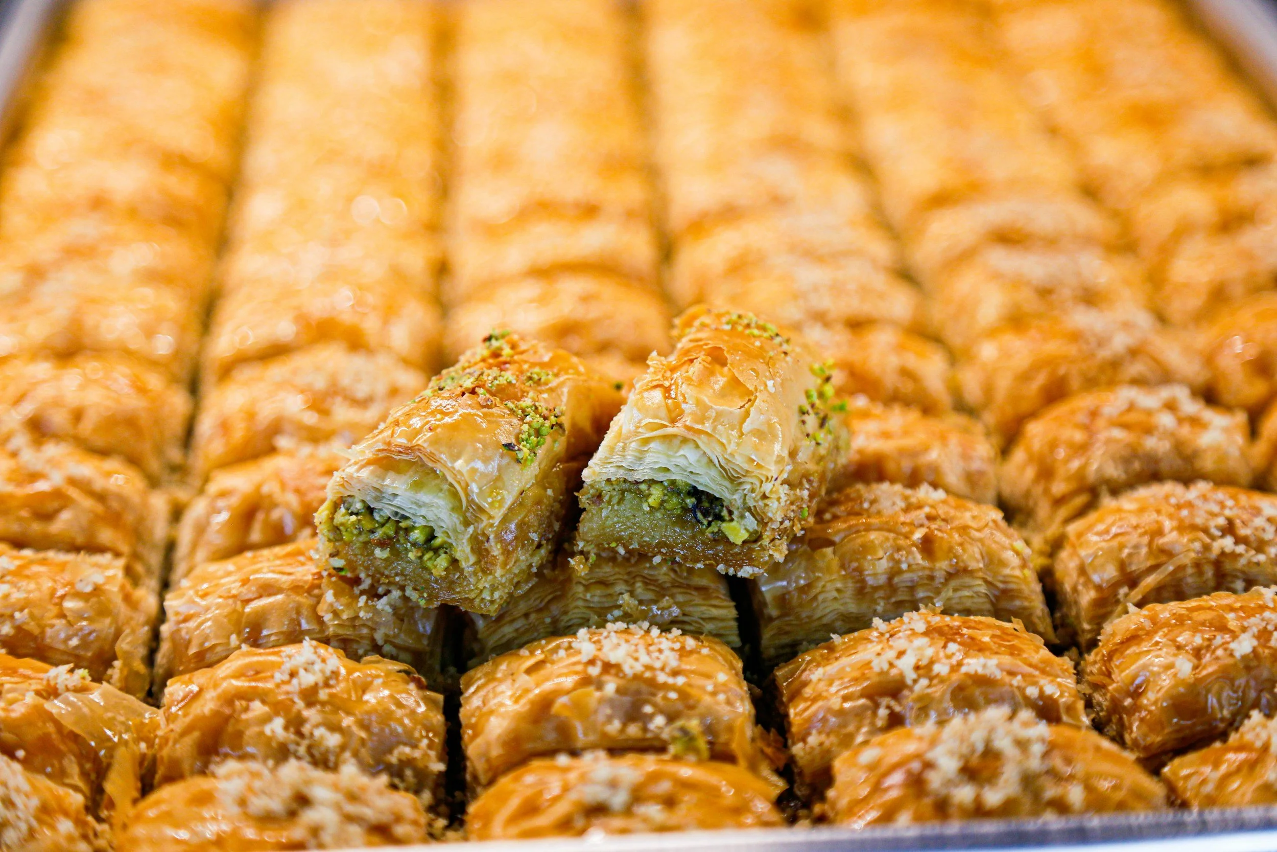A tray of baklava, a layered pastry with chopped nuts and honey, seen with one piece broken in half showing the nut filling inside.