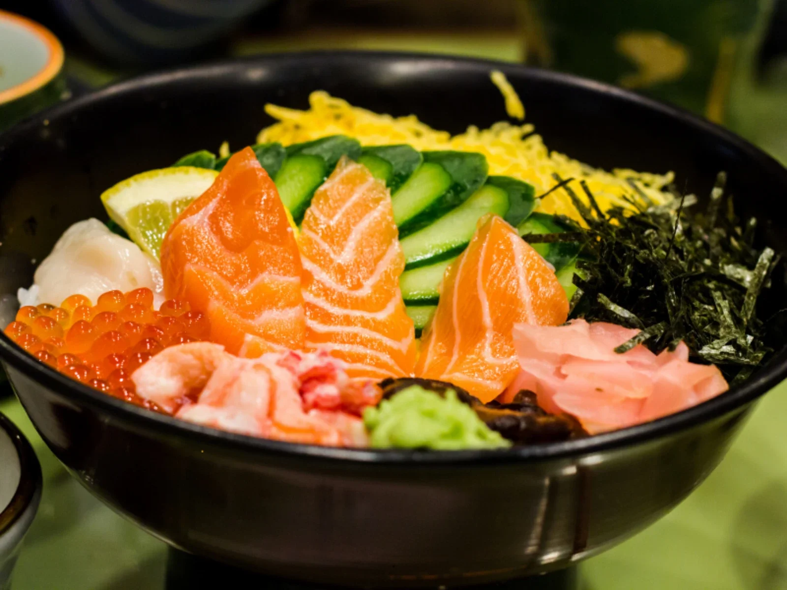 A bowl of assorted sashimi and sushi ingredients including salmon, shrimp, salmon roe, cucumber, shredded nori, and sliced fish on a bed of rice.