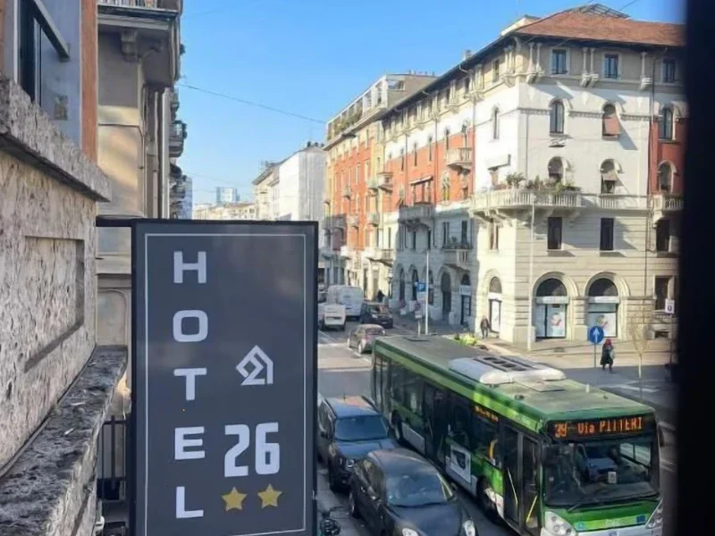 A city street with a green bus, cars, and pedestrians. Buildings with diverse architecture are on both sides, and a blue sky is overhead.