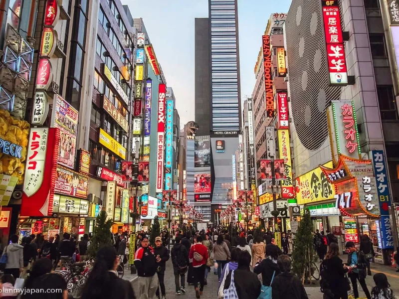 Busy street in Tokyo at night with many neon signs and advertisements in Japanese, crowded with pedestrians.