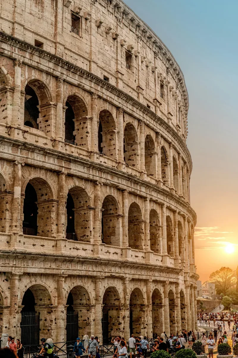The Colosseum in Rome, Italy, during sunset with tourists walking nearby.