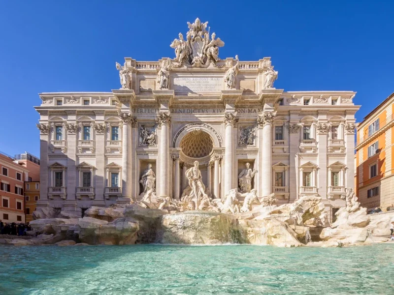 The Trevi Fountain in Rome, Italy, with intricate sculptures and a water basin in the foreground, under a clear blue sky.