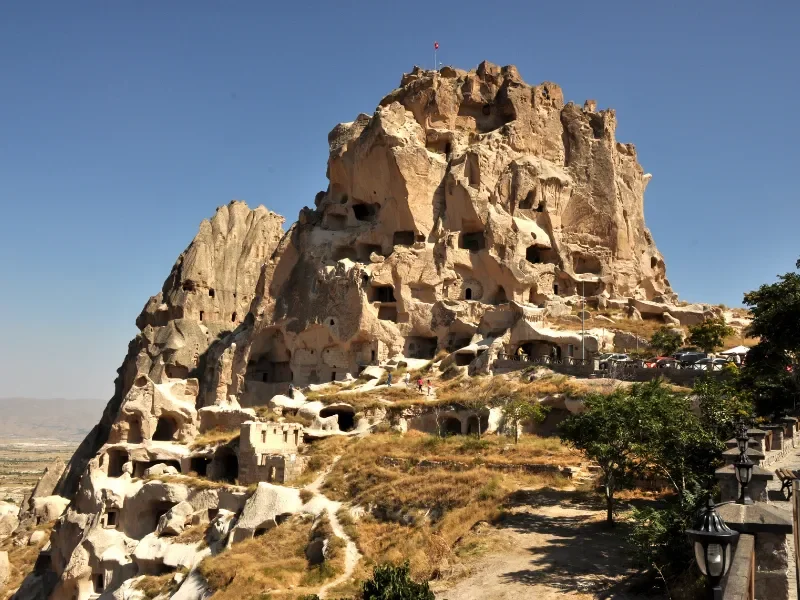 A large rock formation with ancient cave dwellings carved into its side, under a clear blue sky.