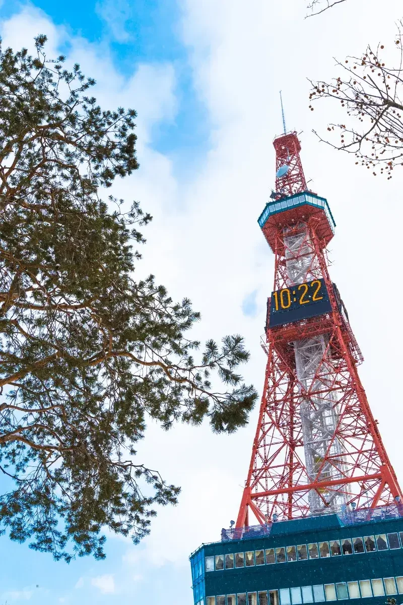 A tall red and white communications tower with a digital clock showing 10:22, against a partly cloudy sky with some trees nearby.