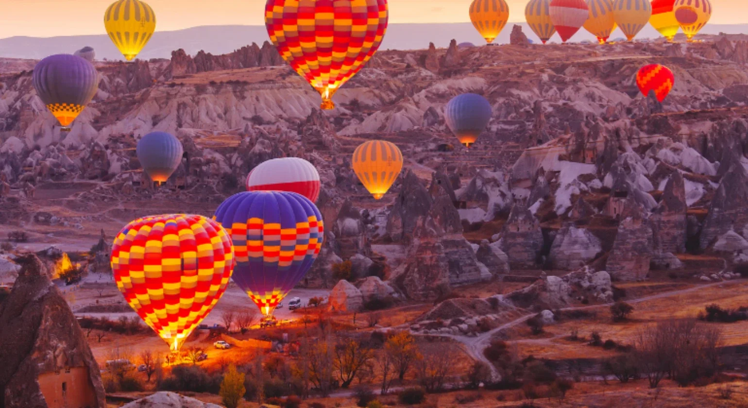 Multiple colorful hot air balloons floating over unique rock formations at sunrise in Cappadocia, Turkey.