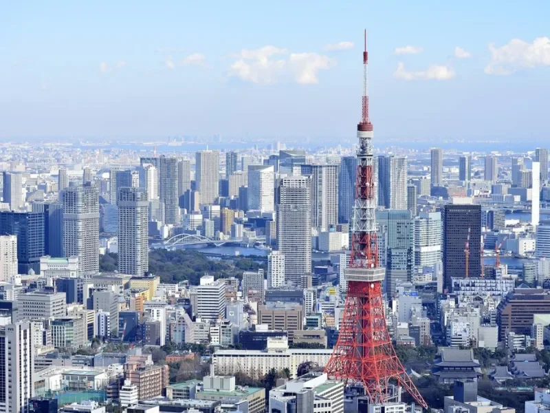Aerial view of Tokyo skyline with Tokyo Tower in the foreground and numerous skyscrapers under a partly cloudy sky.