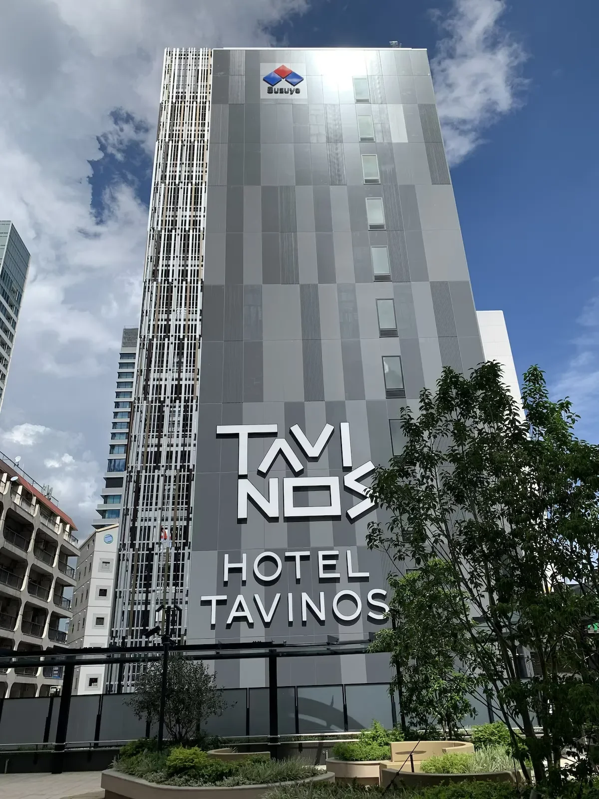 Tall modern building with the sign 'TAVINOS HOTEL' on the front, and a logo with the word 'SUBWAY' at the top, under a partly cloudy sky.