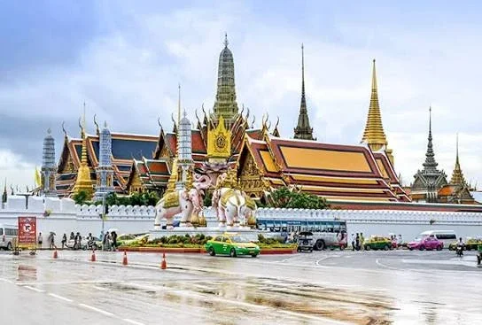 Historic temple complex with ornate architecture and guardians, seen from a street with moving vehicles.