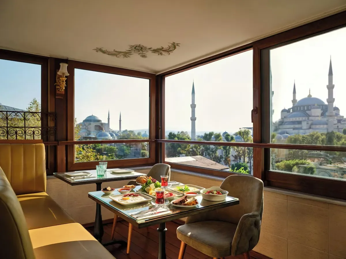 A dining table with plates of breakfast food, set near large windows with a view of a mosque with domes and minarets.
