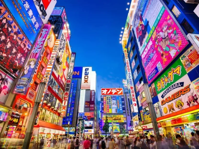 Brightly lit electronic billboards and signs in an urban street with pedestrians in Tokyo, Japan.
