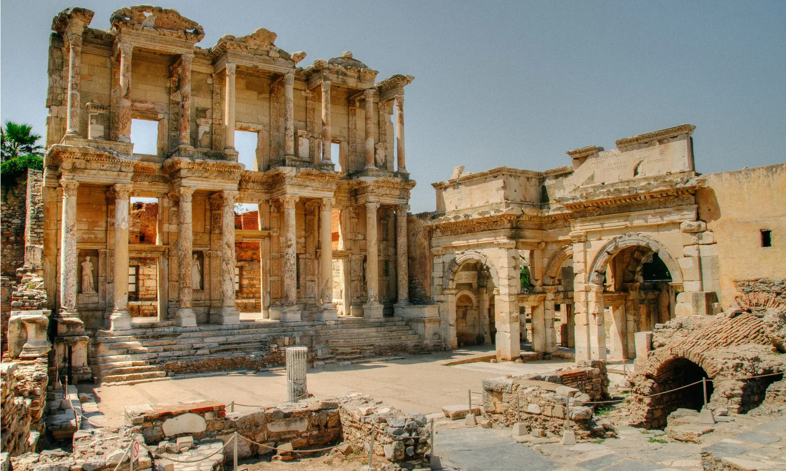 Ancient ruins of a Roman theater with multiple levels of stone columns and arches under a clear blue sky.