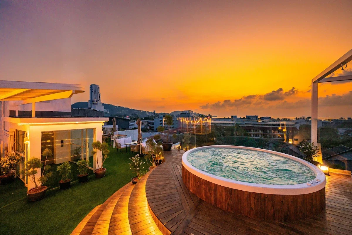 Rooftop view at sunset with a hot tub, outdoor seating, and cityscape in the background.