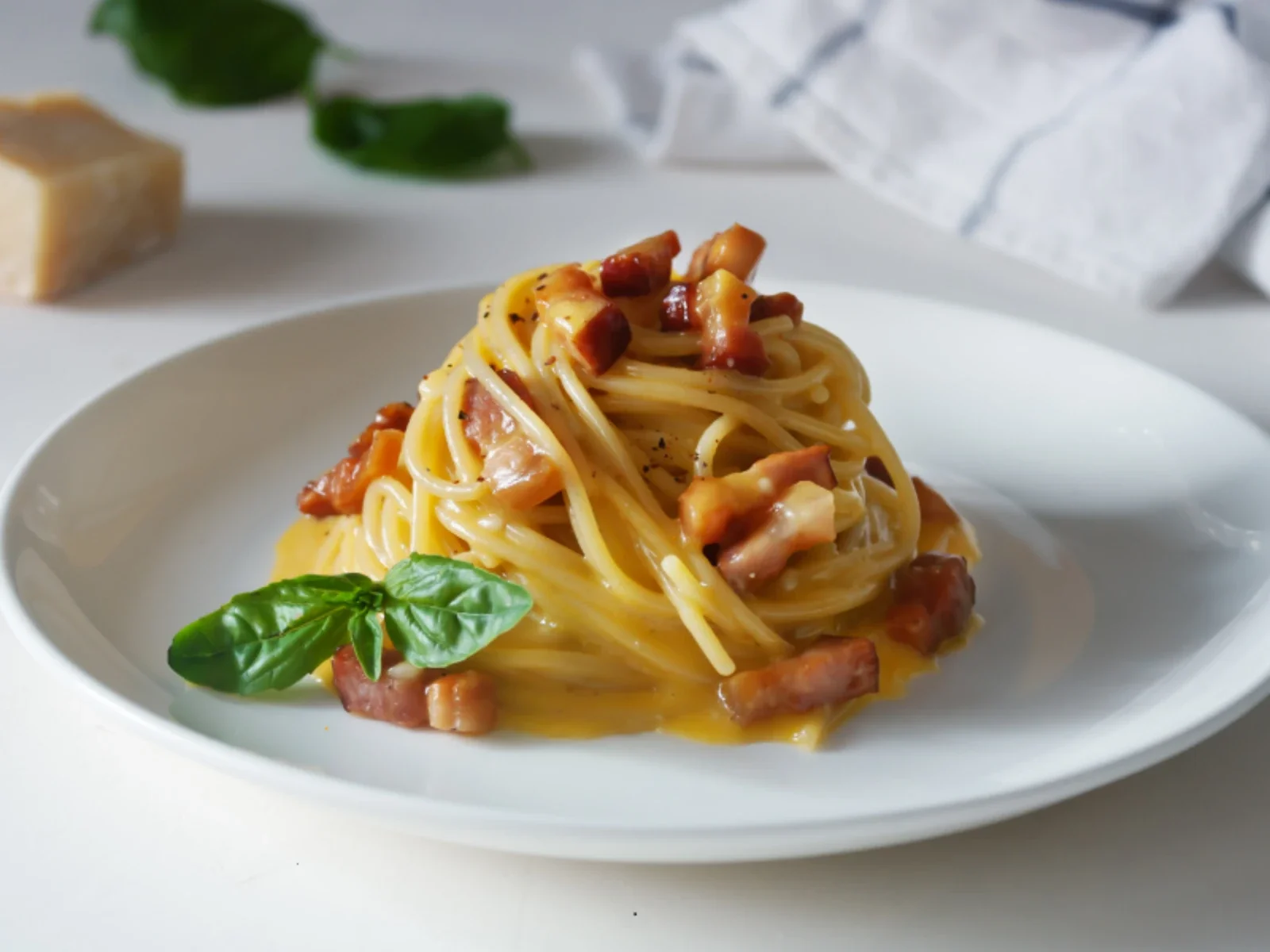 A plate of spaghetti pasta topped with pieces of bacon, garnished with a sprig of basil, served on a white oval dish.