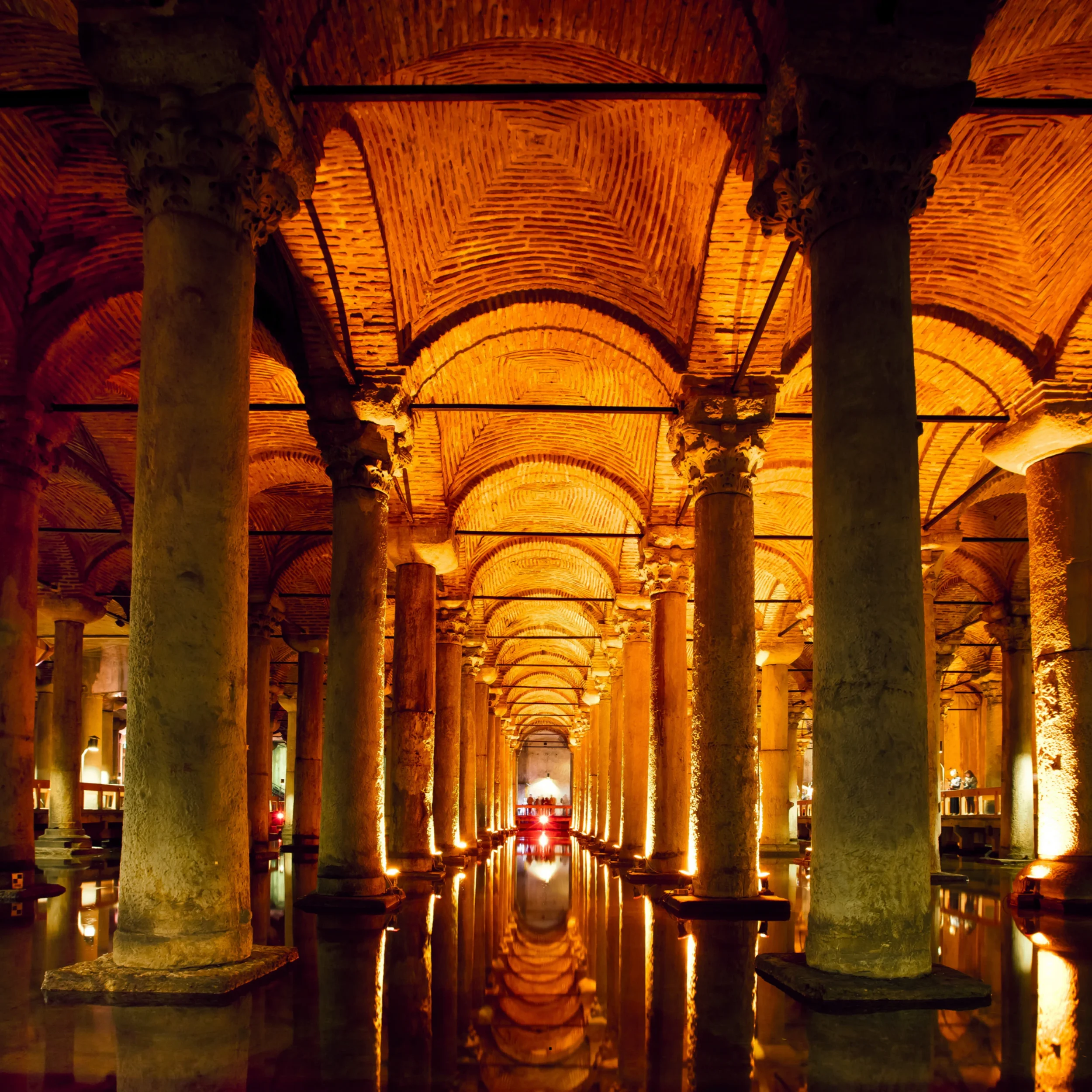 Ancient stone columns and vaulted brick ceilings in a dimly lit underground tunnel, with reflection in a pool of water on the floor.