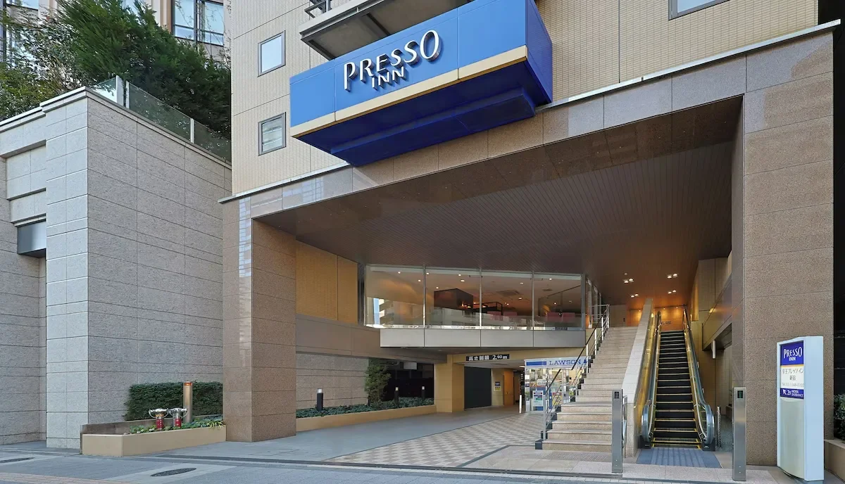 Entrance of the Presso Inn hotel with stairs and an escalator beside a glass-walled area.
