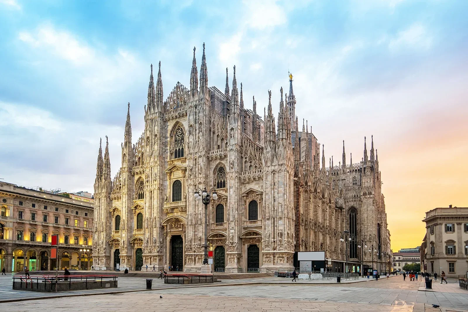 Exterior view of Milan Cathedral (Duomo di Milano) at sunset with people walking in the square.