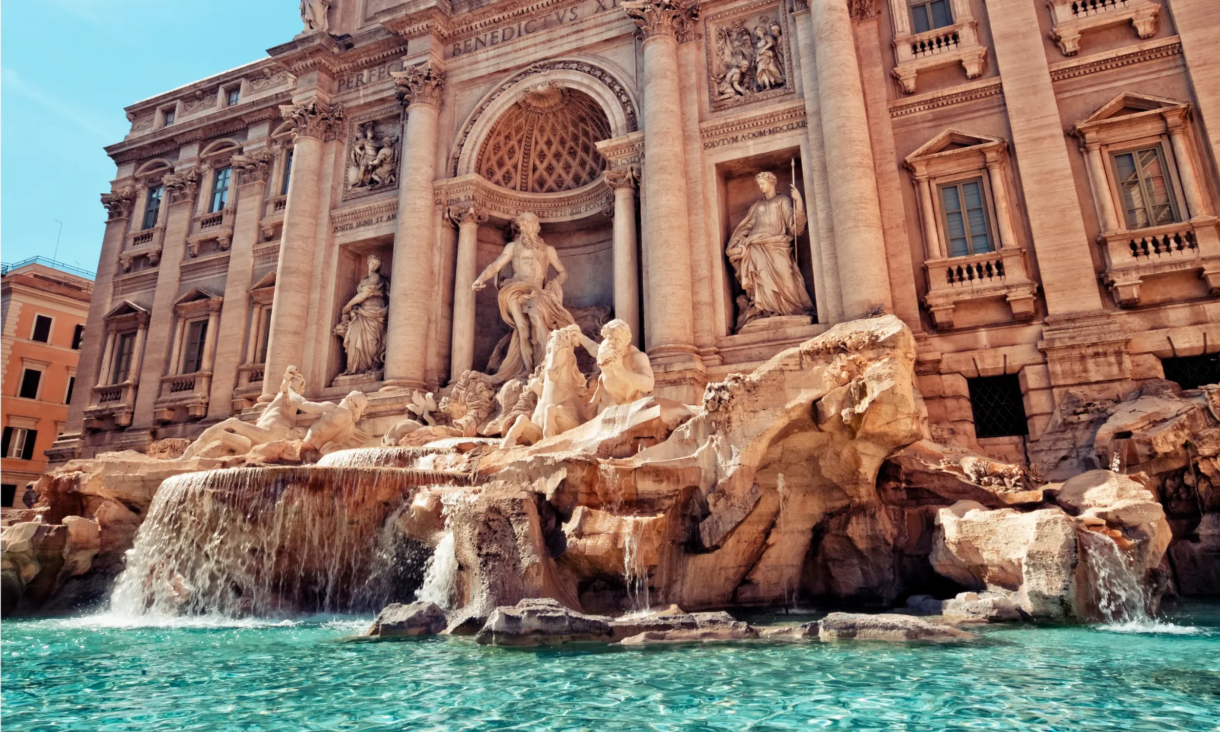 The Trevi Fountain in Rome, Italy, with intricate sculptures and cascading water, set against historic stone buildings.