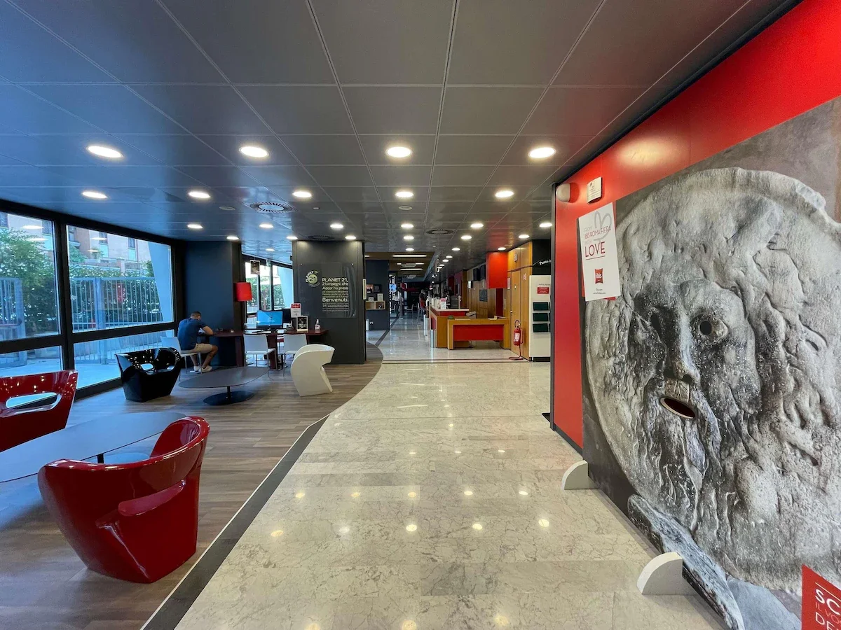 Interior of a modern public space or lobby with seating area, large windows, decorative art, and pathways.