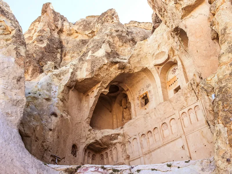 Ancient cave dwelling carved into rock with architectural details, set against rugged cliffs.