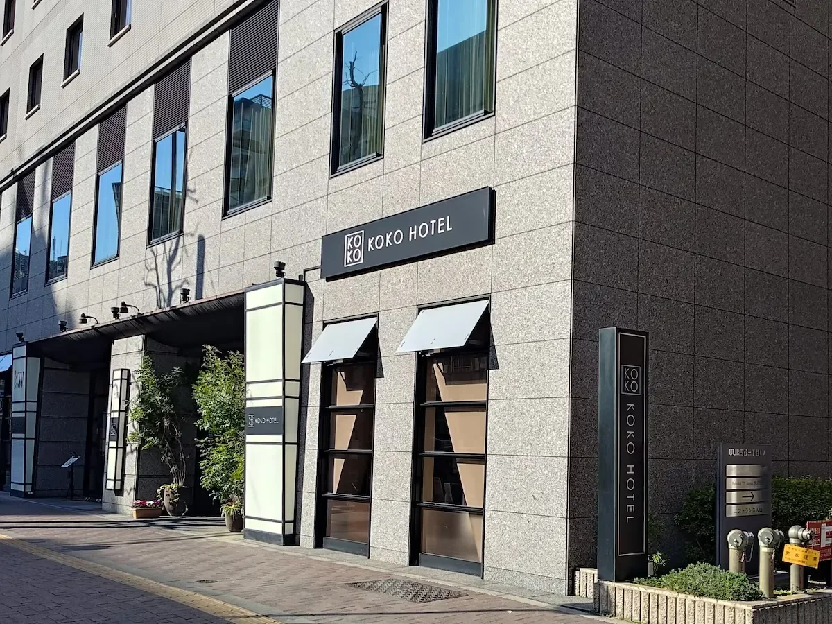 Exterior of a modern hotel building with signs indicating "KO KO HOTEL" and entrance with plants and awnings.