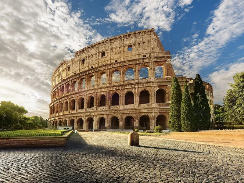 The Colosseum, an ancient Roman amphitheater, with a partly cloudy sky above and trees around it.