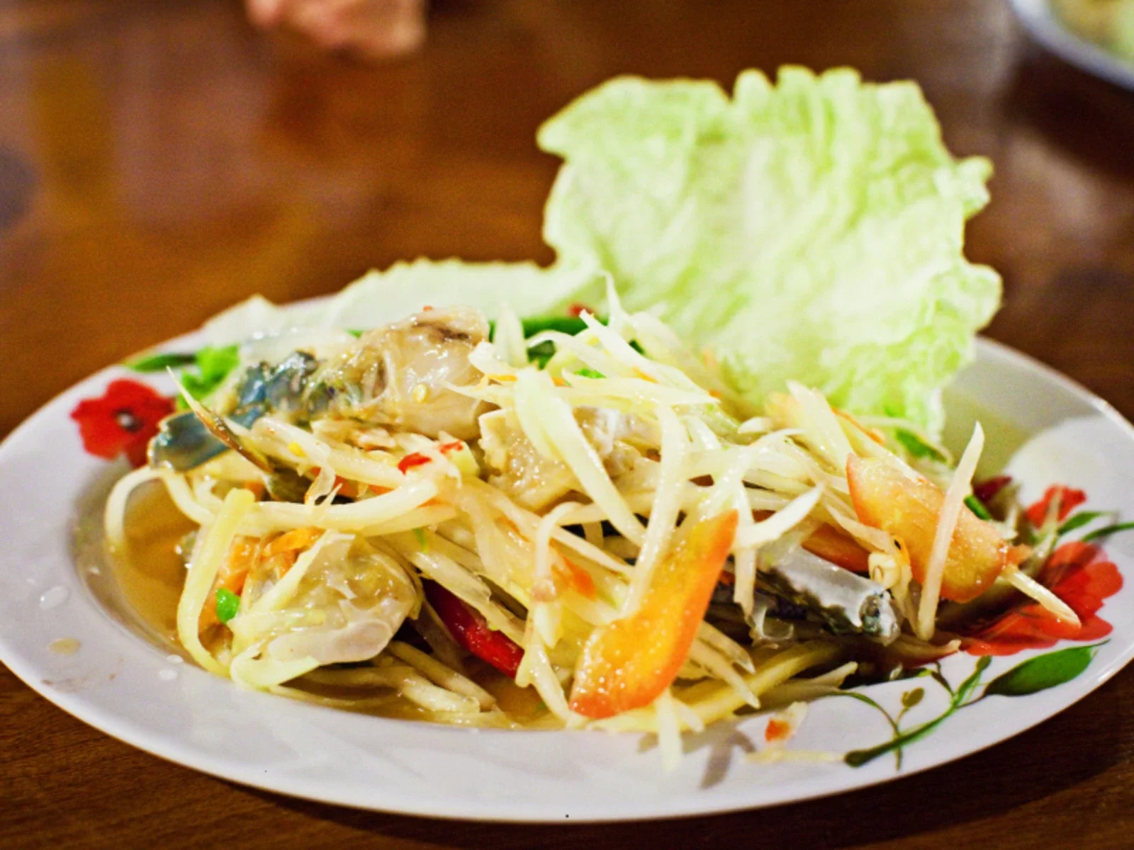 Plate of papaya salad with shredded vegetables and a large lettuce leaf on the side.