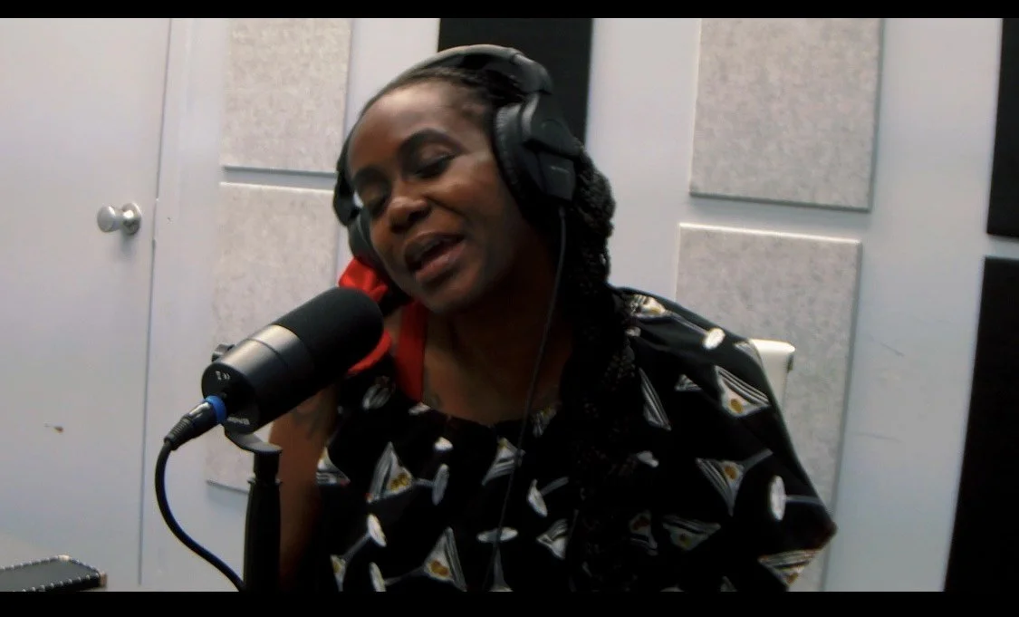A woman wearing headphones singing into a microphone in a recording studio.