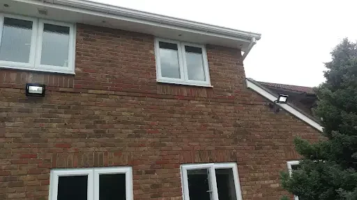 A brick house with two white-trimmed windows on the upper floor and two windows on the lower floor, surrounded by some trees.