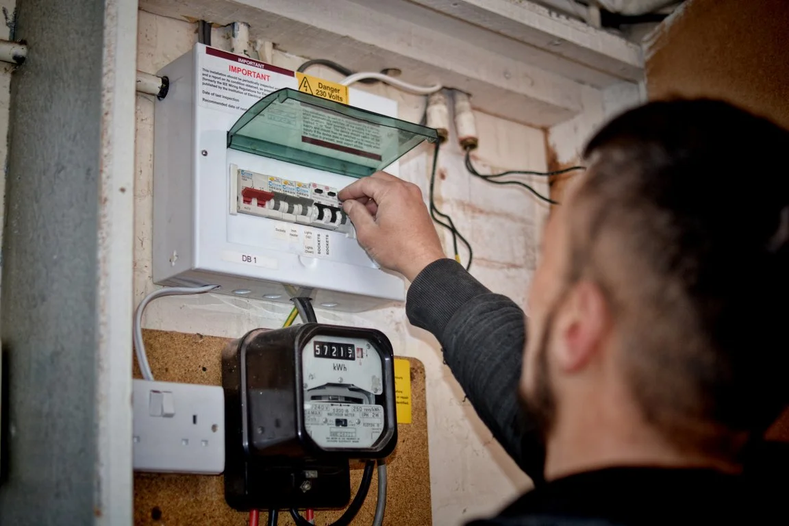 A person adjusting circuit breakers in an electrical panel next to an electric meter on a wall.