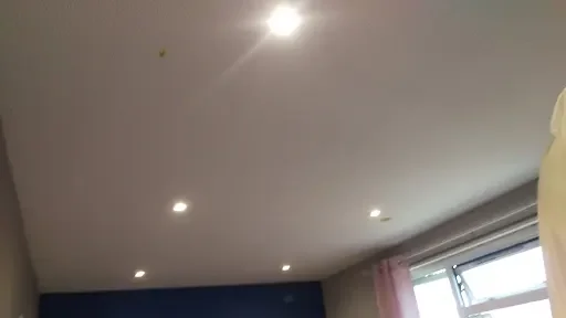 Ceiling with recessed lights and a window with pink curtains.