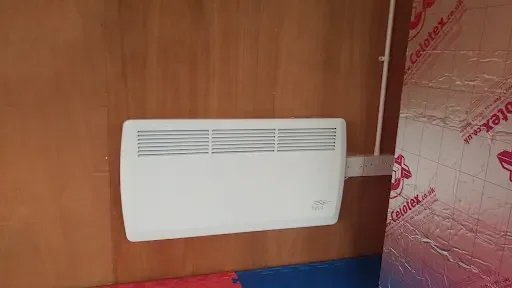 Wall-mounted white heater or radiator with an electrical cord plugged into an outlet.