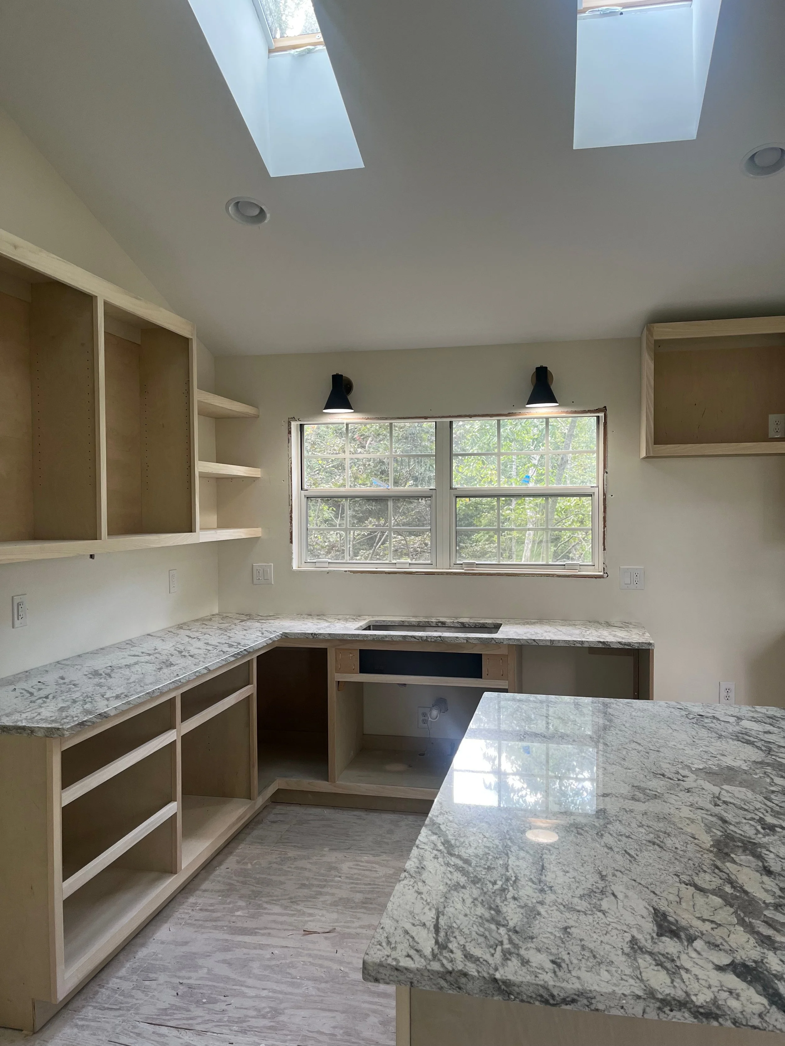 Kitchen mid-renovation with granite countertops installed over unfinished cabinet boxes