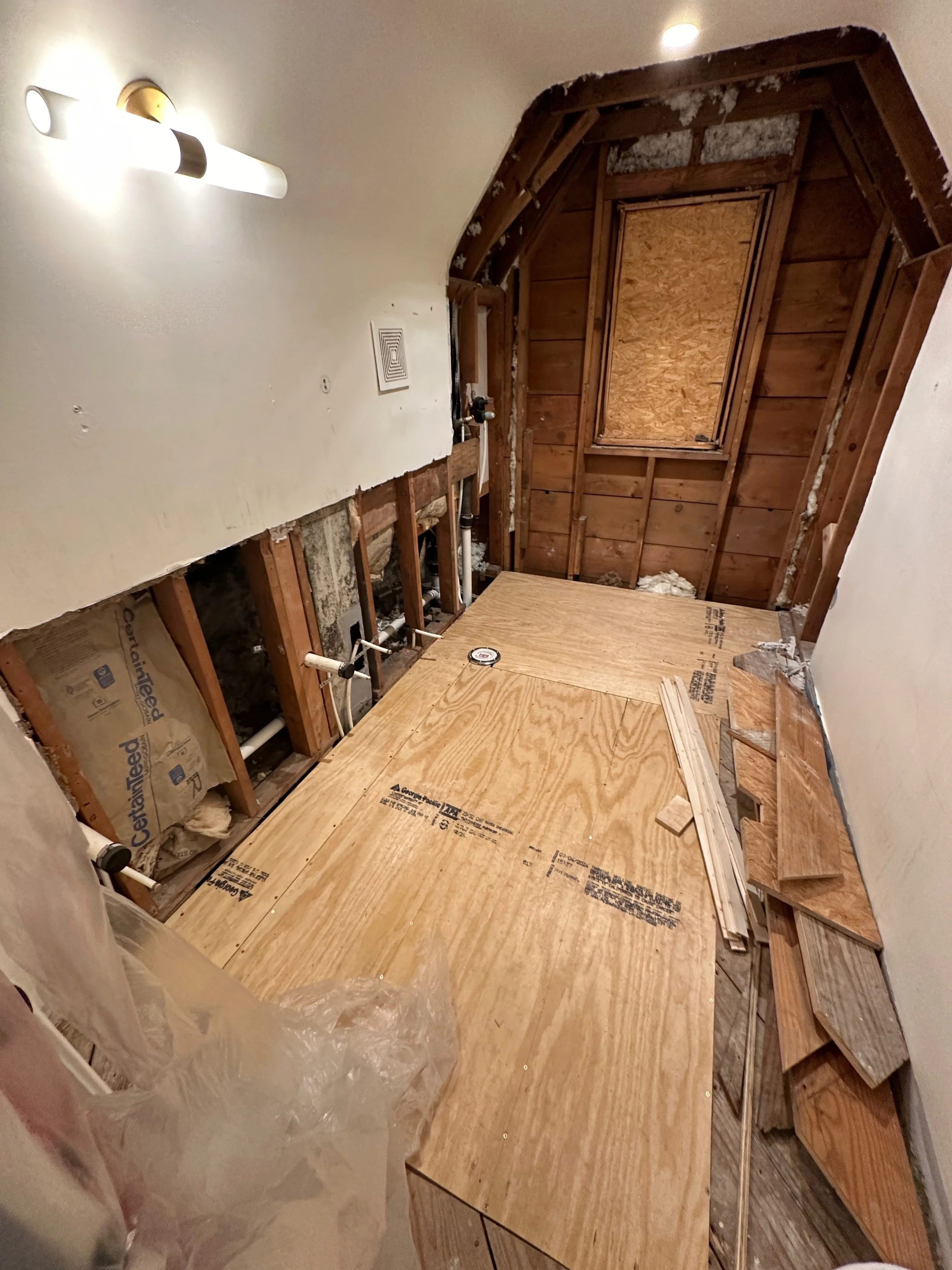 Bathroom renovation showing exposed framing and plywood subfloor before finishing