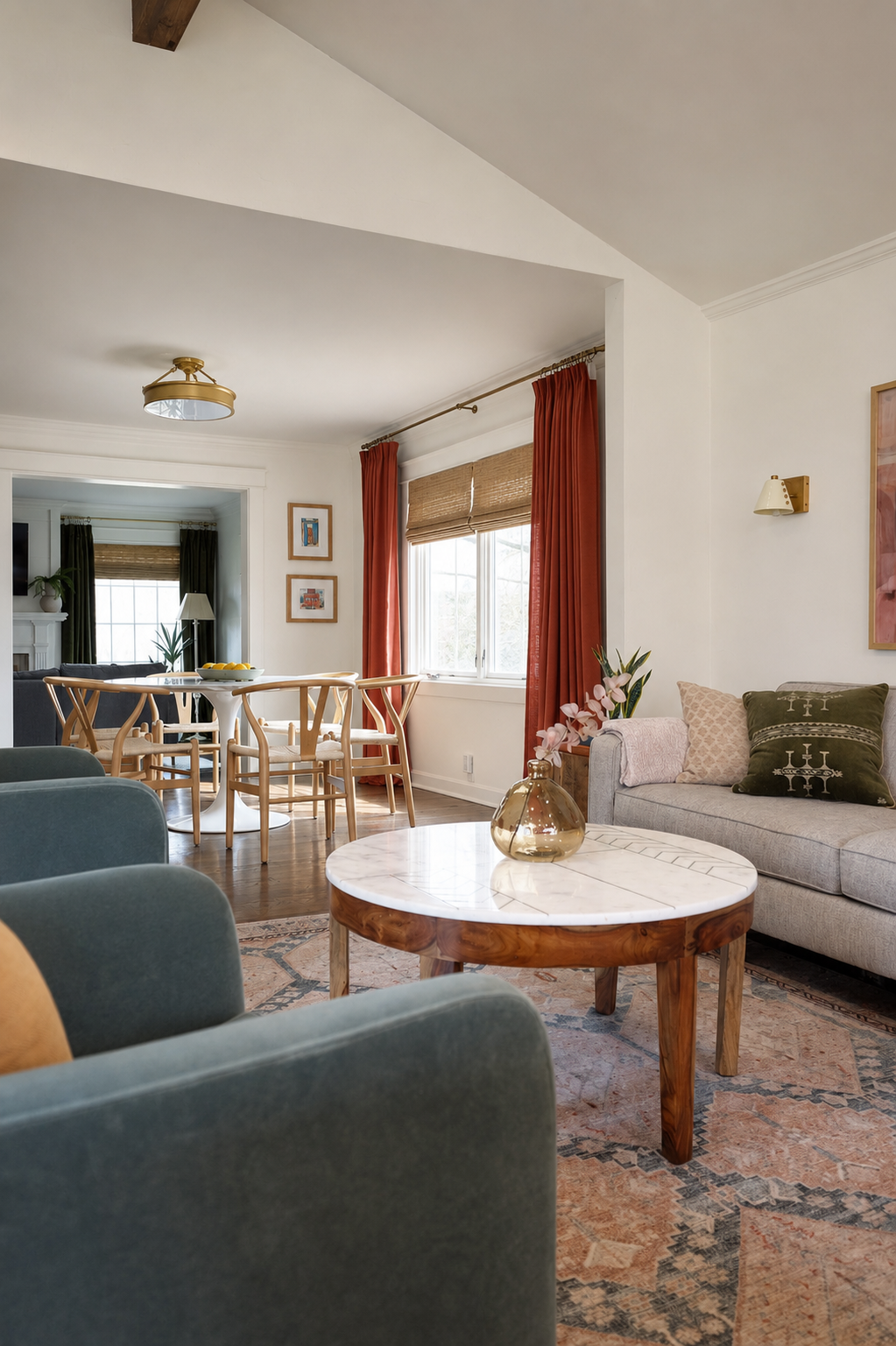 Living room with vaulted ceiling opening into a dining nook, framed by rust curtains and woven shades