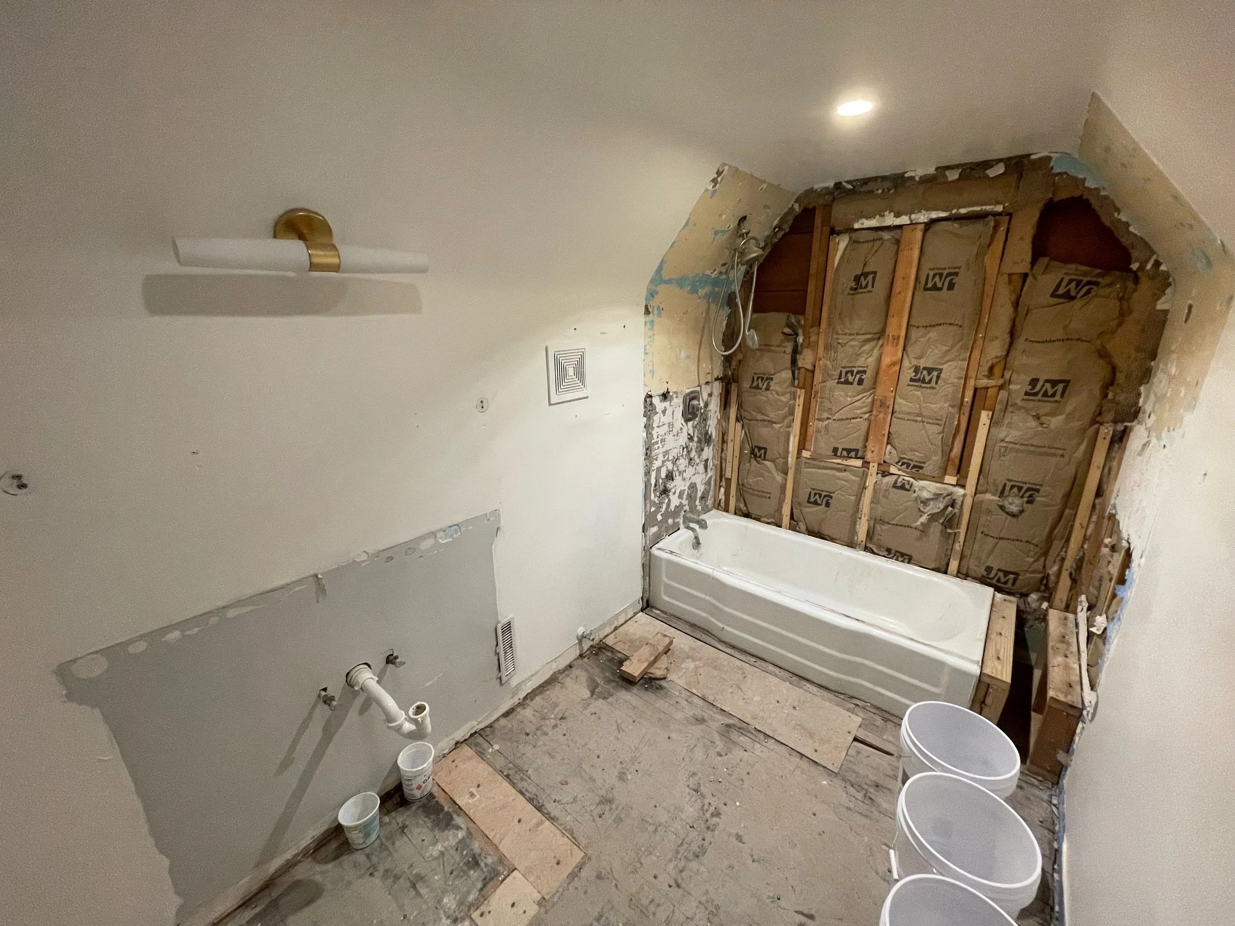 Bathroom mid-renovation with exposed wall studs, insulation, and a freestanding tub