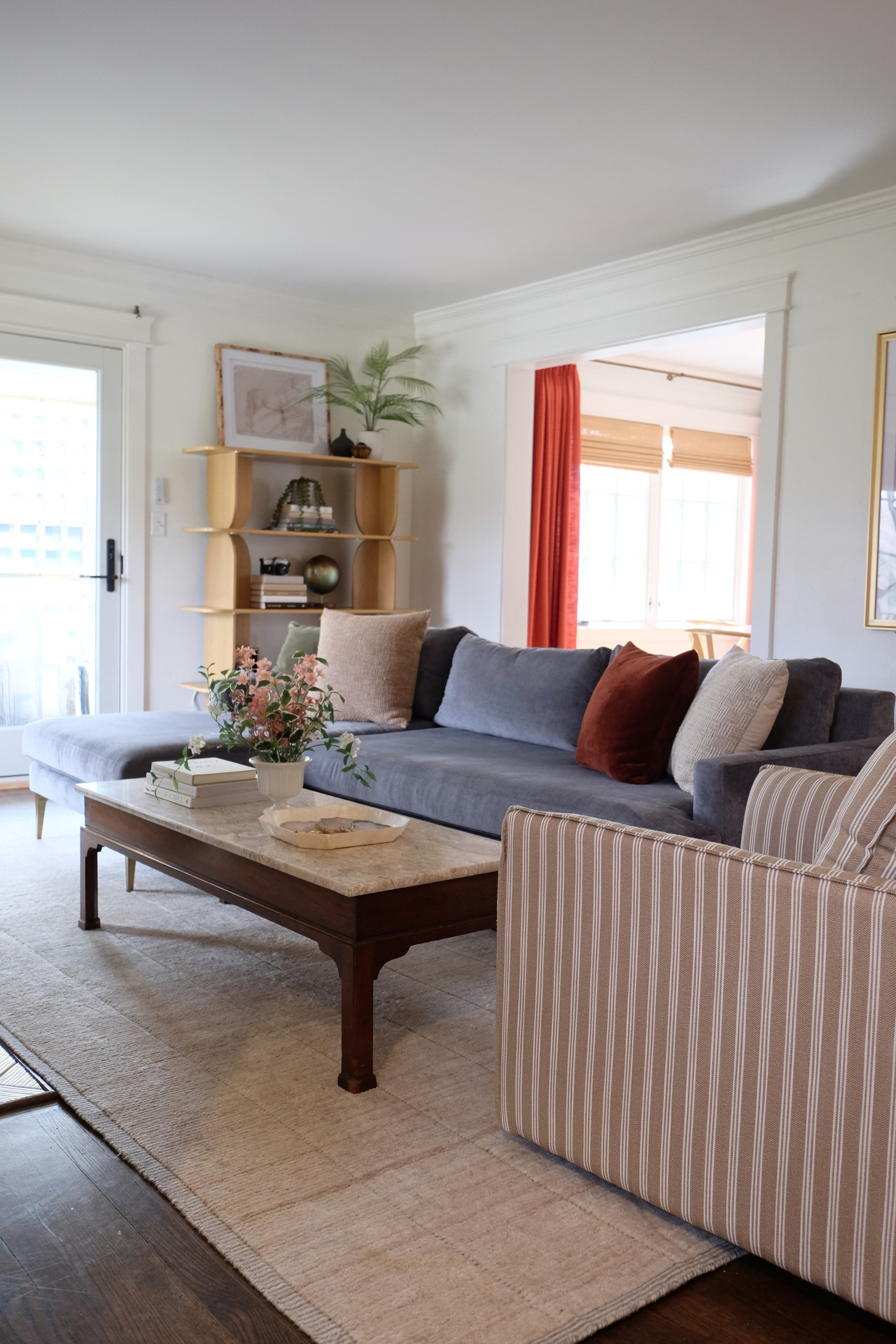 Living room with a blue velvet sectional, striped armchair, and wood coffee table on a patterned rug