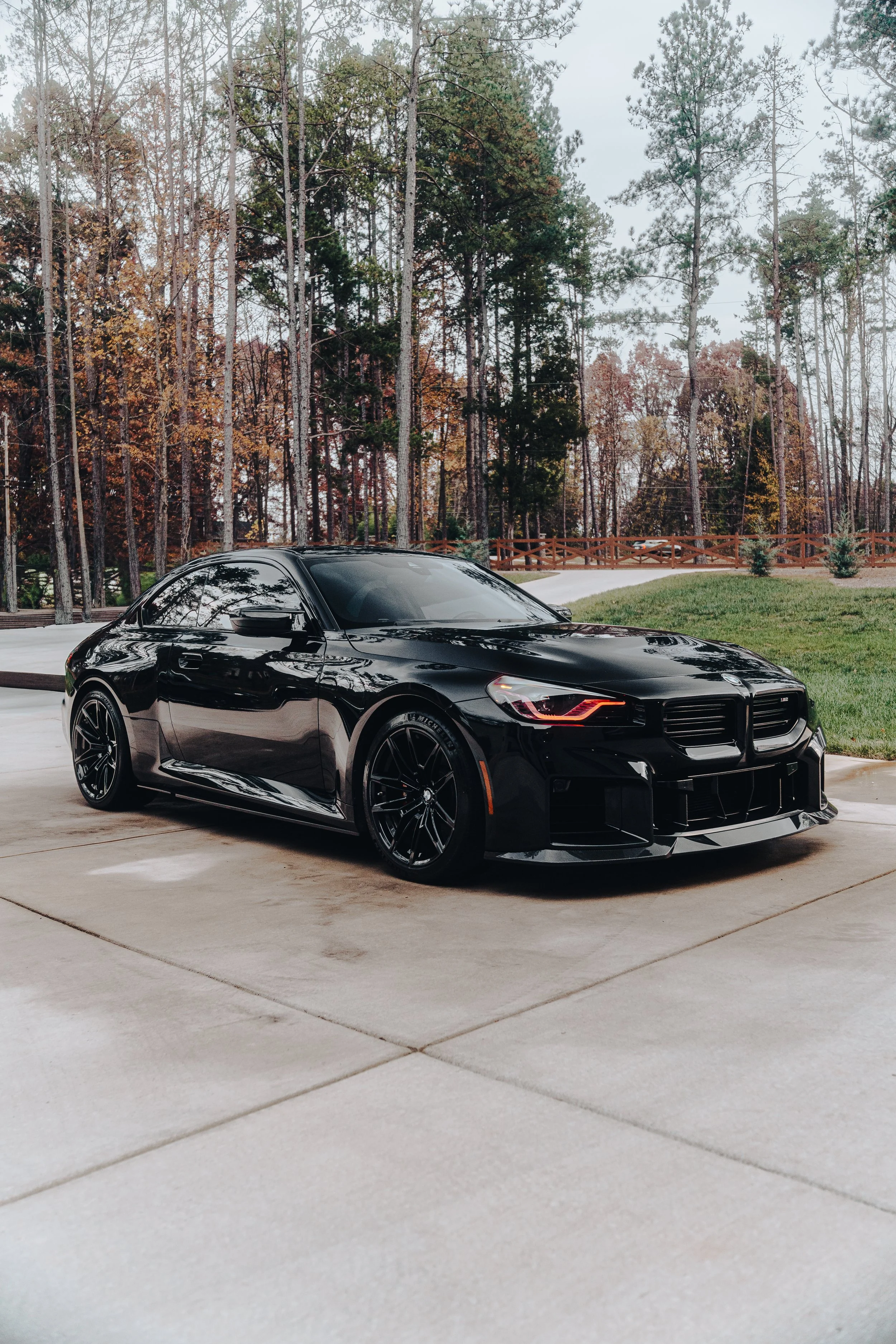 A black sports car parked on a concrete driveway with trees and grass in the background.