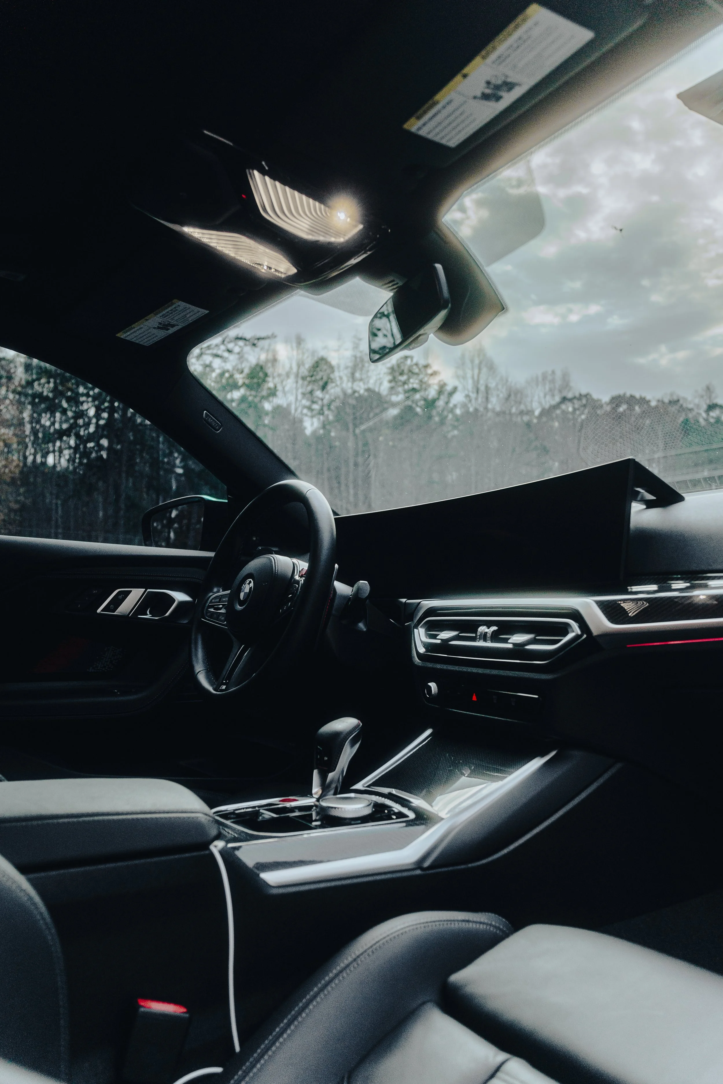 Interior of a modern car with a digital display, steering wheel, gear shift, and window showing a cloudy sky outside.