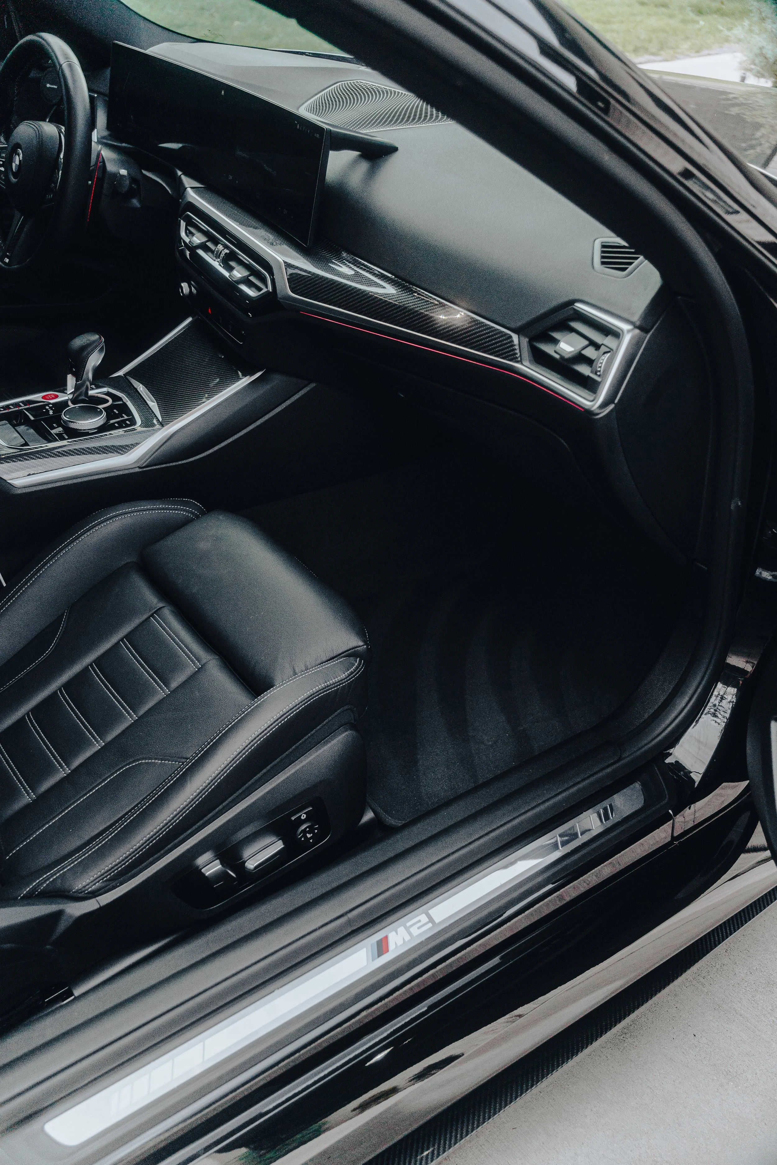 Interior of a BMW M2 car showing the driver's seat, dashboard, and center console with a digital display and gear shifter.
