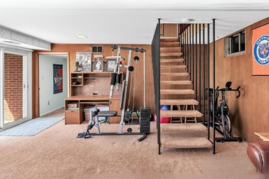 Home gym with exercise equipment, staircase, and sports memorabilia on the wall. This is a "Before" photo that shows a client's home before we renovated it.
