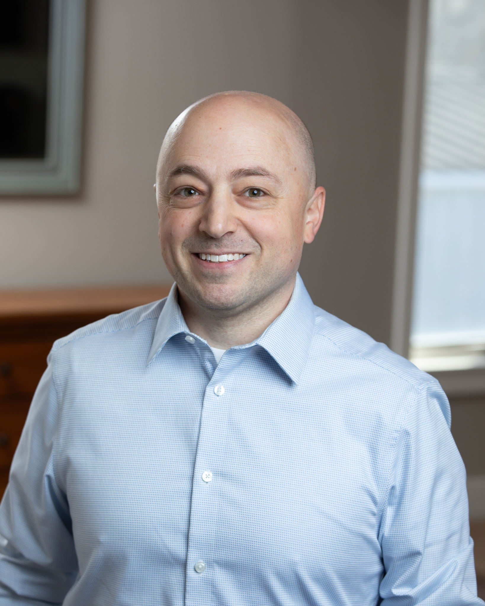 Robert Gray is a smiling middle-aged man with a shaved head wearing a light blue button-up shirt in an indoor setting.