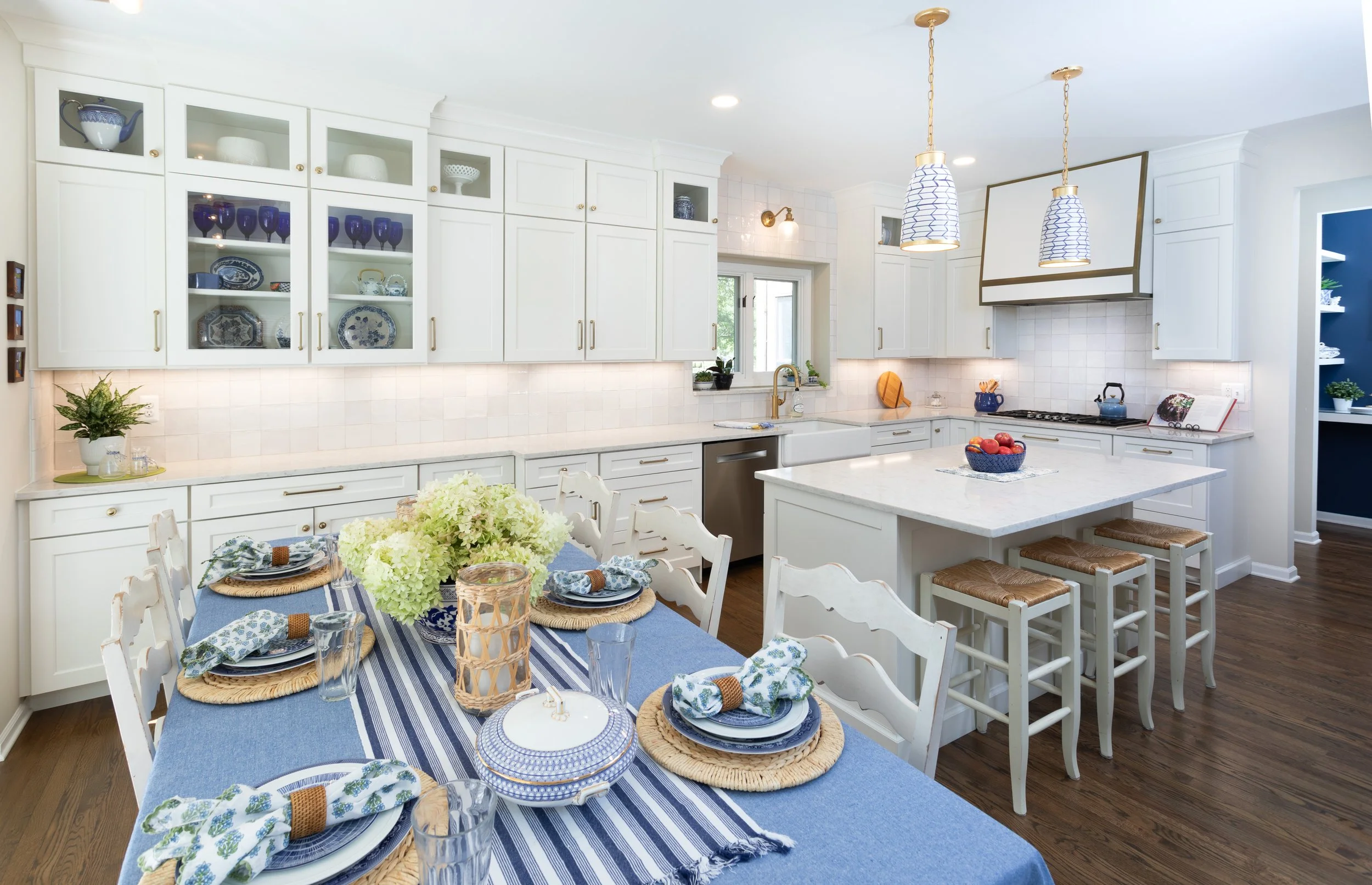 Coastal-style traditional looking kitchen with white cabinets, a marble island, blue accents, and a dining table set with blue and white plates, and woven placemats.