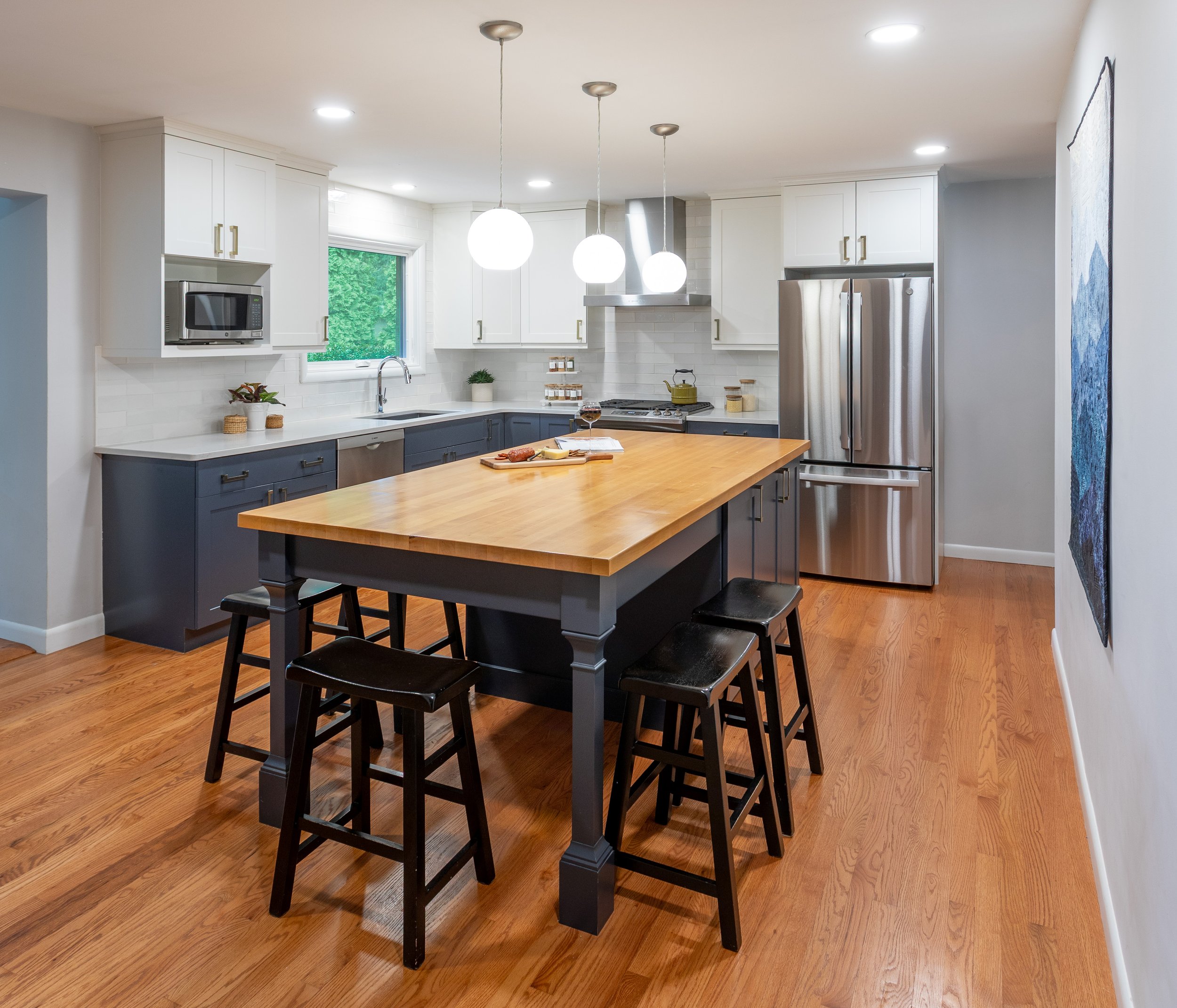 Modern kitchen with white upper cabinets, navy lower cabinets, stainless steel appliances, wooden kitchen island, and hardwood floors.