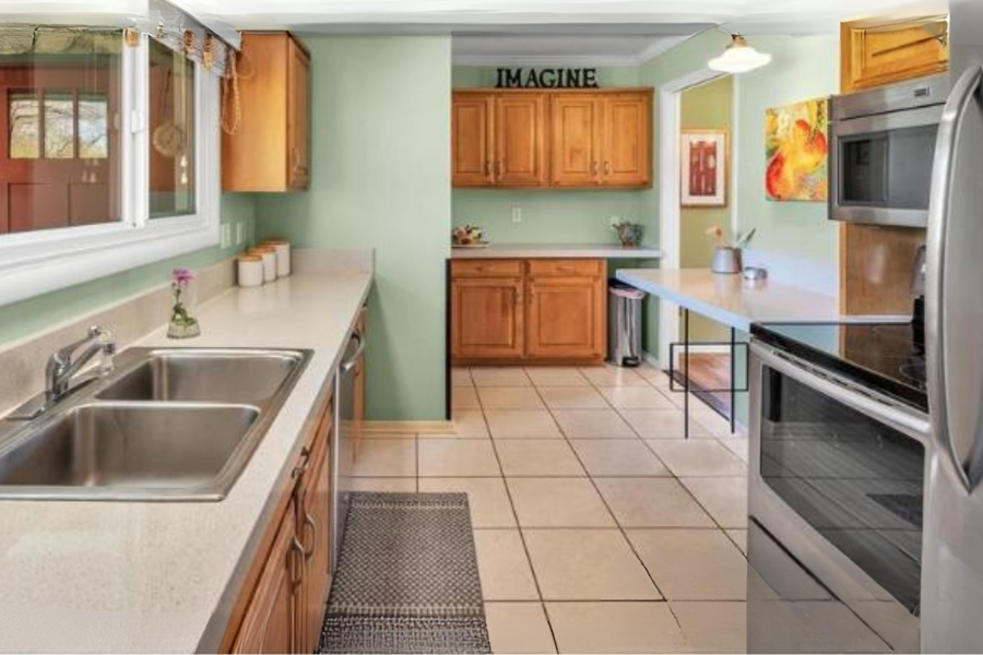 Kitchen with green walls, wooden cabinets, a double sink, stainless steel appliances, a table with chairs, and decorative wall art.