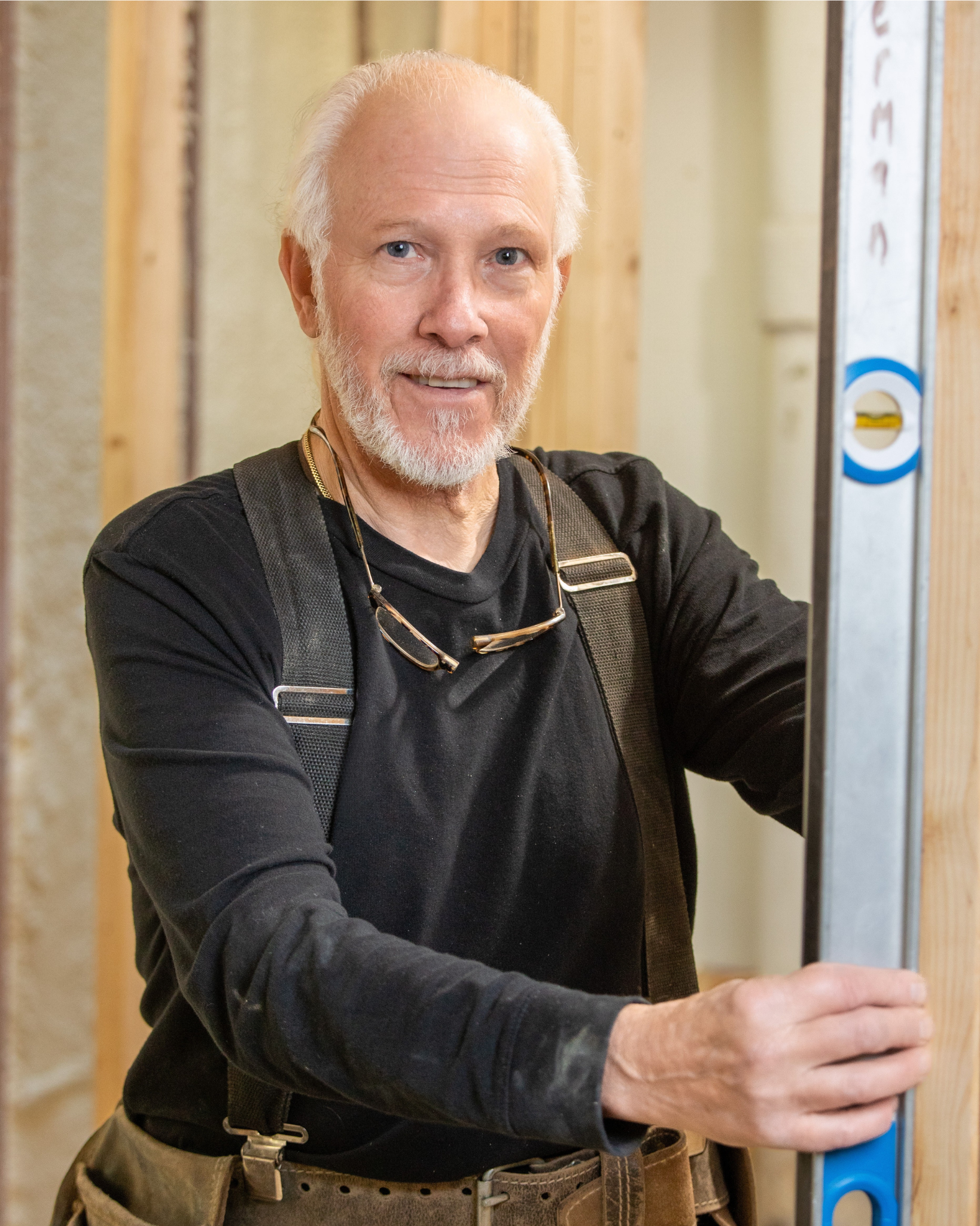 Robert Vipperman is a middle-aged man with a white beard and gray hair working on a construction site, holding a level tool.